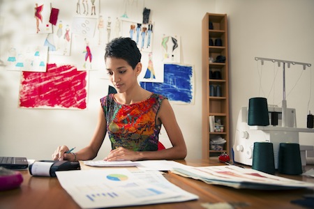 Money and financial planning, young hispanic self-employed woman checking bills and doing budget with calculator, computer and papers in fashion design studio